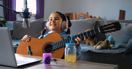 Little girl plays guitar and sings in her video blog, live stream recording, fun for kids, virtual socializing, recording tutorials