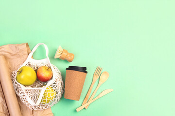 Reusable wooden cutlery, cork mug and grocery bag with apples. Dishwashing brush and kraft wrapping paper, eco friendly fork, knife, spoon on green mint backdrop. Zero waste concept. Copyspace.