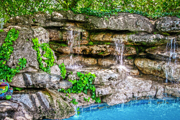 Rock waterfall into swimming pool with grainy sandstone and climbing vines