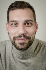Fototapeta premium Portrait of a smiling young brown-haired man with a short beard and a gray turtleneck sweater