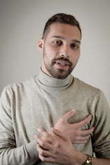 Portrait of a young man with a short beard with with his hand over his heart as a sign of sincerity 