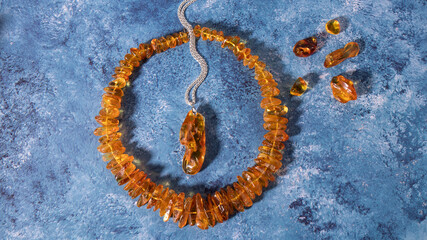 Fototapeta premium Amazing transparent orange amber pendant and necklace on a blue background. Retro composition, flat lay, copy space. 