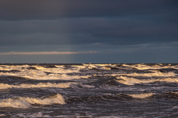 Wavy water of the Baltic sea and sandy shore in the warm evening sunlight. 