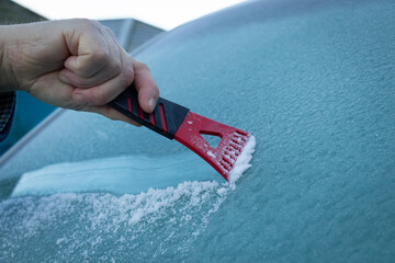 A man scraping ice off a frozen wind shield or screen of a van in the winter