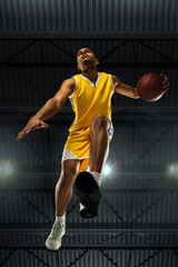 Young professional basketball player in action, motion isolated on black background, look from the...