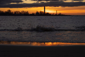 Fototapeta na wymiar View to the Daugavgriva lighthouse from Mangalsala pier against colorful sunset sky