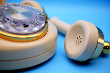 Vintage Rotary Phone Close Up Handset on blue background. Macro view of speaker and dialer. Cream, ivory color with gold metal trim. For concepts related to innovation, communication, old, outdated.