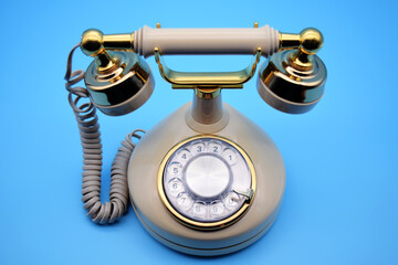 Retro, vintage, antique rotary phone on blue background. Overhead view. Cream, Ivory with gold metal accents. For concepts related to telephones, phones, communication, technology, innovation, and old