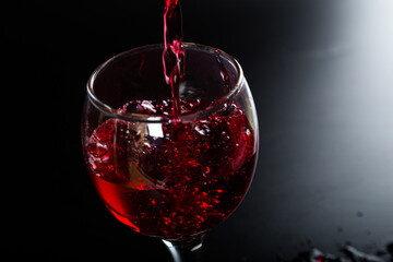 Pouring red wine with splashes and drops into a glass on a black background.