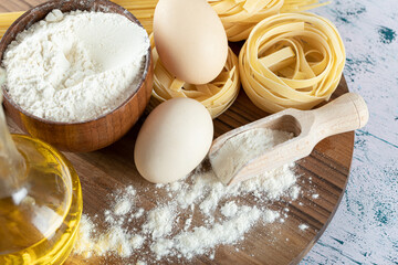 Two kinds raw pasta with oil, egg and bowl of flour on wooden board