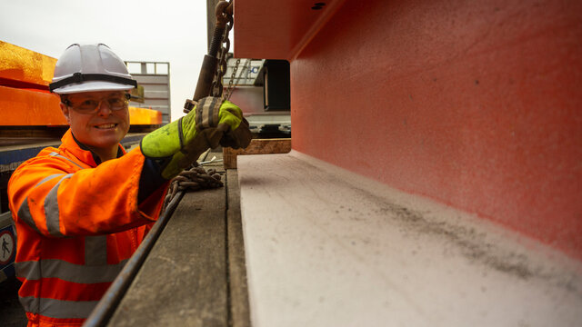 Male Driver in PPE Ratcheting up a steel Chain on a Flatbed Trailer