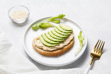Bran bread toast with chickpea hummus and avocado on white stone table background. Close up
