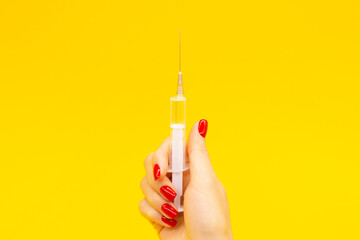 A woman's hand with a fashionable red manicure holds a syringe on a yellow background. The concept of medicine