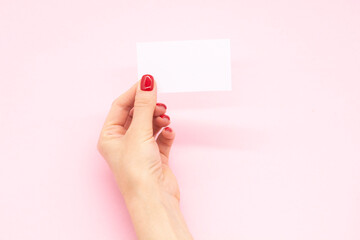 Woman's hand with fashionable red manicure holding business card on a pink background . Summer spring nail design.