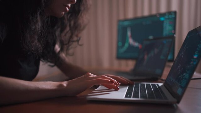 young female trader with laptop and screen looking at stock charts