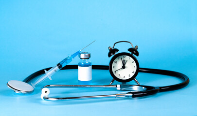 Blue syringe with coronavirus epidemic vaccine and clock on blue background