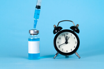 Close-Up Of Coronavirus Vaccine With Alarm Clock On Blue Background