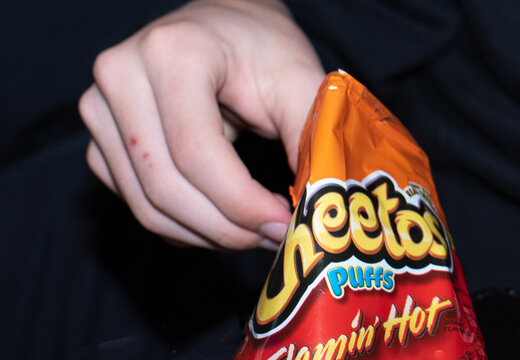 Boy eating Flaming Hot Cheese Puffs with Cheese on his fingers.
