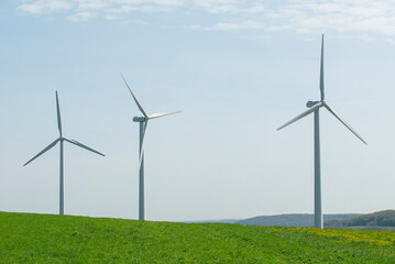 three wind towers rise up from behind a green field