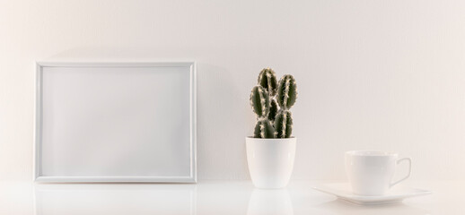Modèle de cadre photo blanc avec espace vide pour logos, inscription publicitaire. Cadre en mode paysage sur un espace de travail avec une tasse et des plantes vertes.	