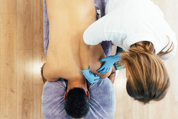 Top view of a treatment in a physiotherapy clinic. Female Physiotherapist performing a dry needling treatment on the bare back of a patient in pain.