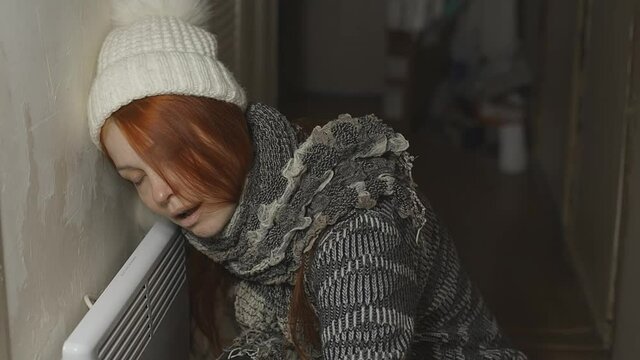 a woman is warming herself at the radiator in a cold house, problems with heating, heating the room with an electric convector