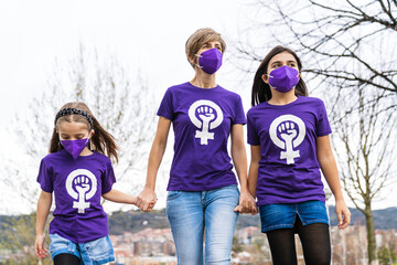 mother and daughters walking down the street and wearing a purple T-shirt with the symbol of working women on International Women's Day, March 8, and wearing a mask for the coronavirus pandemic