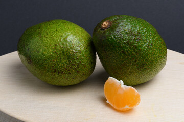 Two avocados and a slice of tangerine on a cutting board