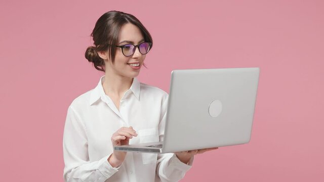 Funny young business woman in white shirt glasses posing isolated on pink background studio. Achievement career wealth concept. Working on laptop pc computer making video call conducting conversation