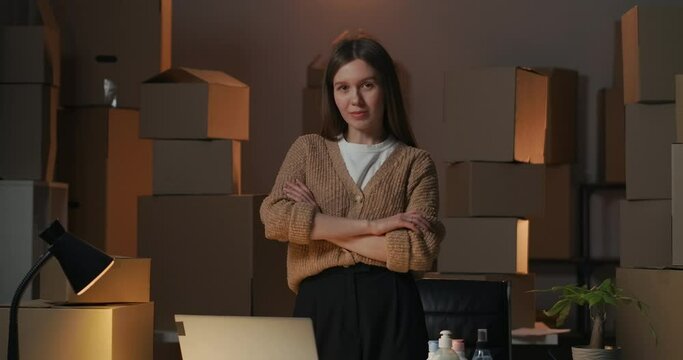 portrait of confident businesswoman, owner of online shop with cosmetic goods at home warehouse at evening, medium shot
