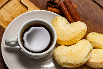 Xícara de café com biscoito de queijo e pau de canela sobre a mesa.