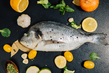 fish with lemon and vegetables. Delicious fresh fish on black dark  background. Fish with aromatic herbs, spices and vegetables on a black table. healthy food, diet, cooking concept. Prepare fish 