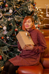 Beautiful happy woman sitting next to Christmas tree with with a gift in her hands