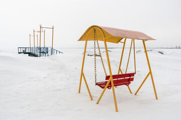 An old swing against the background of a snowy shore..