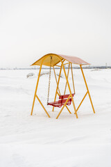 An old swing against the background of a snowy shore.