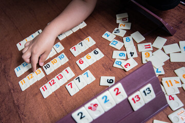 Kid playing Rummy with game tiles laid on a plastic rack simulating wood, in a mosaic style
