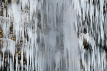 Fototapeta na wymiar Beautiful long icicles of a frozen waterfall, with water flowing and crashing down and Ice water dripping from the tips of icicles in a cold eery and moody atmosphere in a cave in the mountains 