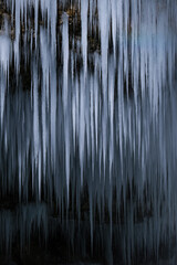 Beautiful long icicles of a frozen waterfall, with water flowing and crashing down and Ice water dripping from the tips of icicles in a cold eery and moody atmosphere in a cave in the mountains 