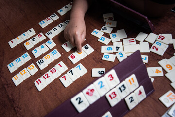 Naklejka premium Kid playing Rummy with game tiles laid on a plastic rack simulating wood, in a mosaic style 