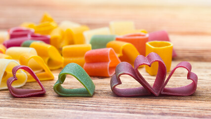 Pasta heart shaped on a natural wooden table. Raw dry Italian pasta. Orange, yellow, red, green colors. Food for holidays. Love symbol Valentine's Day. 