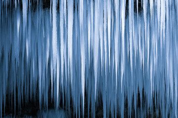 Beautiful long icicles of a frozen waterfall, with water flowing and crashing down and Ice water dripping from the tips of icicles in a cold eery and moody atmosphere in a cave in the mountains 