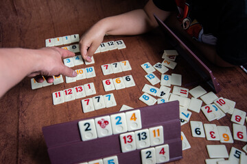 Kid playing Rummy with game tiles laid on a plastic rack simulating wood, in a mosaic style
