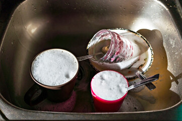 unwashed dishes in soapy foam in metal kitchen sink, housework
