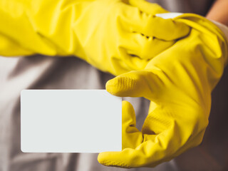 Man in gray robe puts on yellow rubber gloves and holds white card with copy space. Cleaning services for premises or announcement of sale in store of household supplies and crop production.