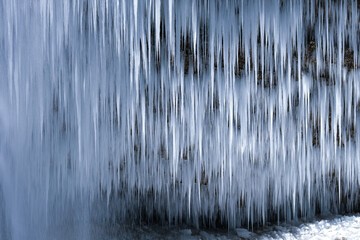 Beautiful long icicles of a frozen waterfall, with water flowing and crashing down and Ice water dripping from the tips of icicles in a cold eery and moody atmosphere in a cave in the mountains 
