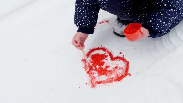 winter fun. child draws with paints in the snow. close-up. drawing on the snow. have fun on snowy winter day, outdoors.