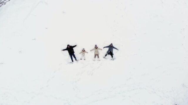 winter family fun. Happy family of 4 are making angels on the snow. aero, top view. Family is enjoying of snow and snowfall, having fun on snowy winter day, outdoors.