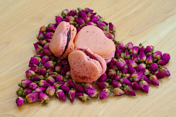 Pink heart homemade macaron cookies filled with raspberry jam for Valentines Day on a dried roses background
