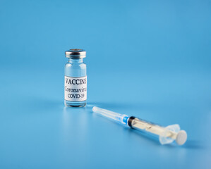 Coronavirus vaccine: a syringe and a bottle on a blue background. The concept of immunization and vaccination. Copyspace.