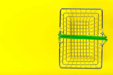 Metal basket on yellow background for shopping in supermarket, view from top.